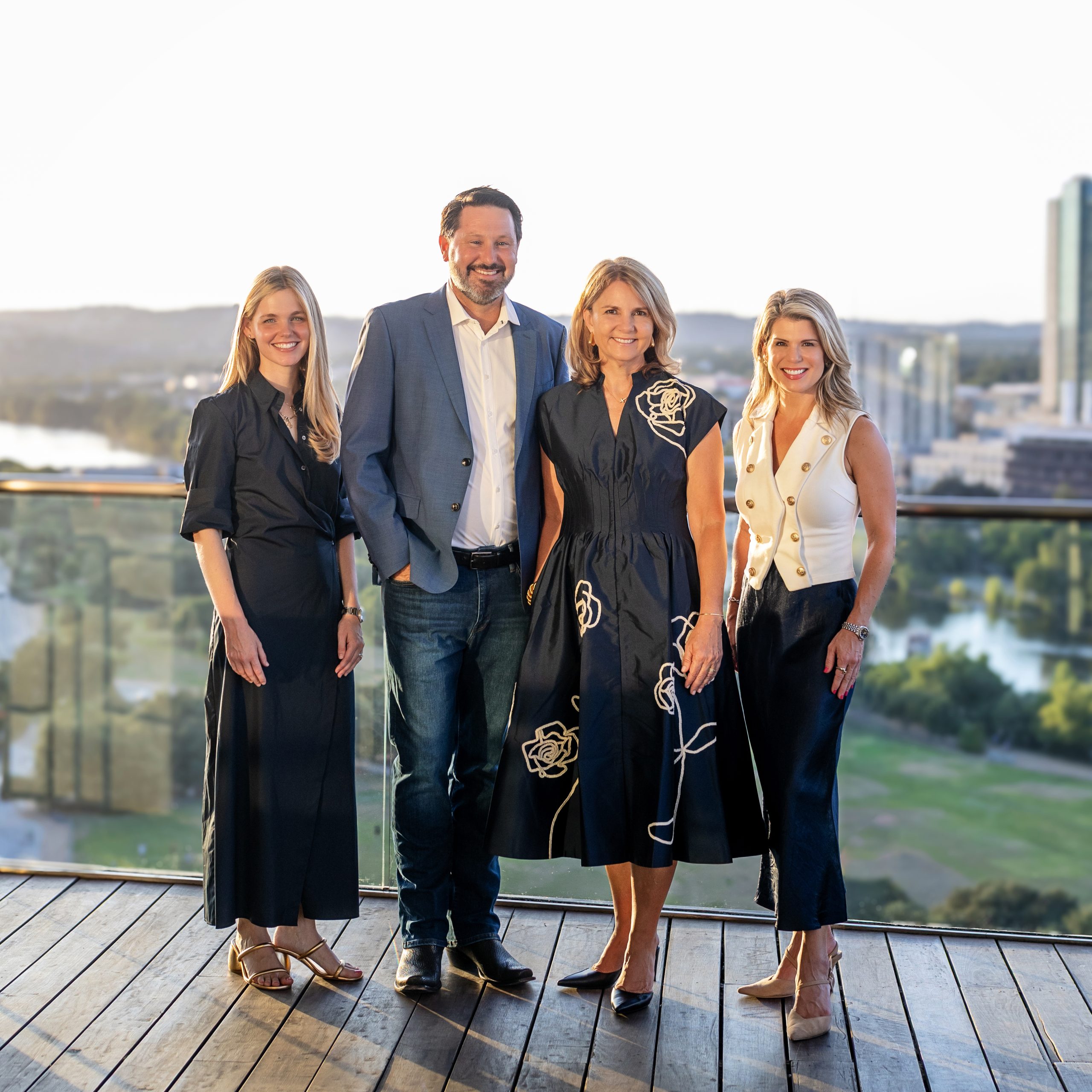 Four members of the Moreland Properties sales team standing on a deck above Lady Bird Lake with the Austin skyline behind