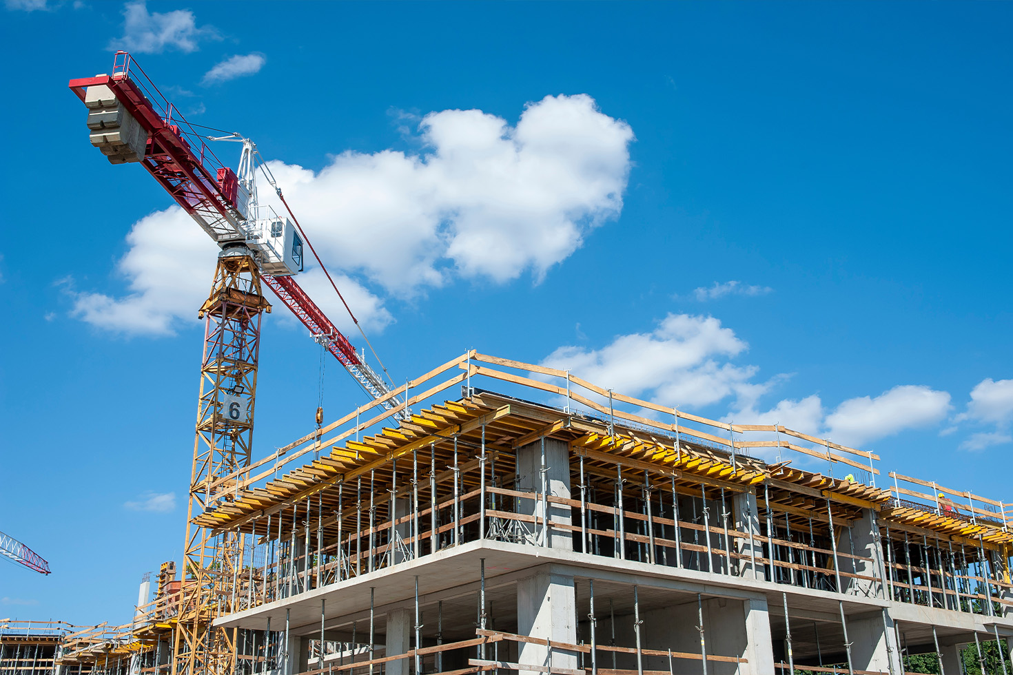 The concrete superstructure of the tower under construction beneath a red tower crane against a blue sky