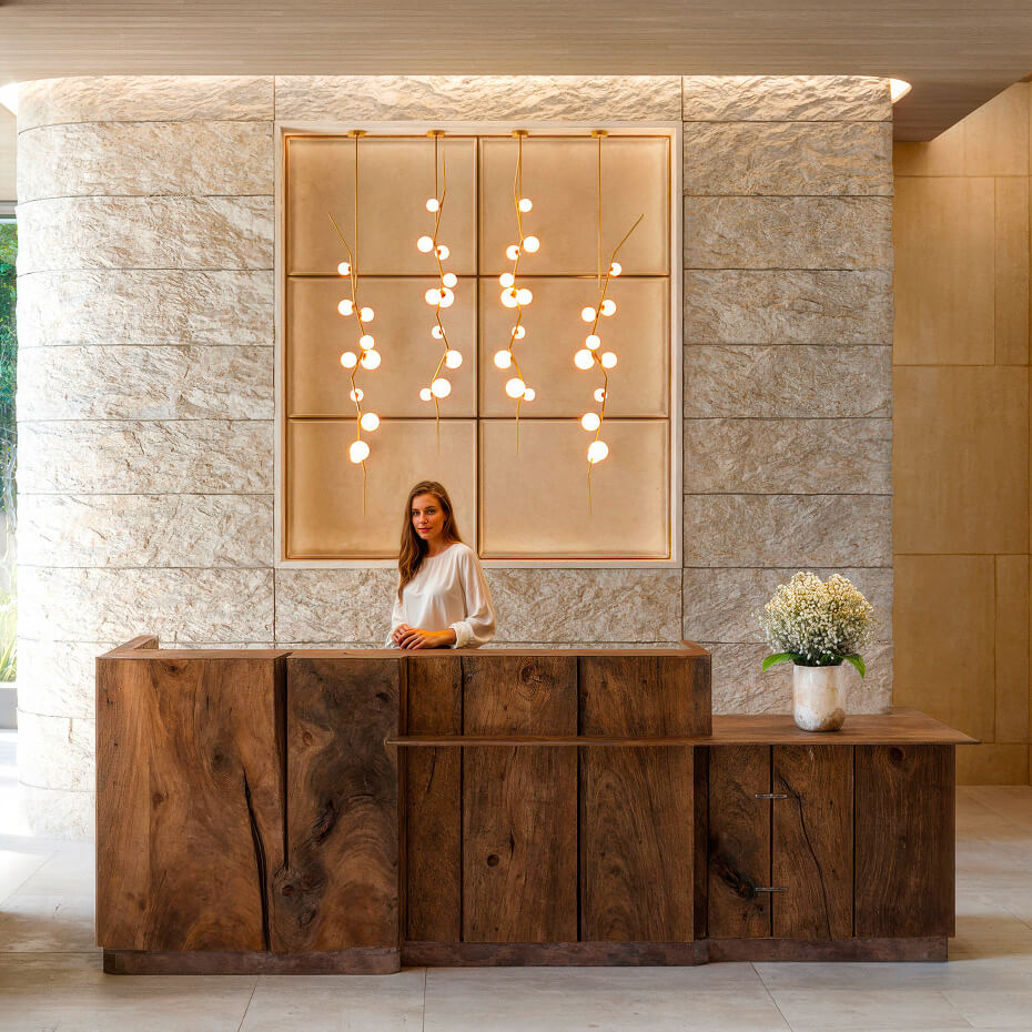 Rendering of the lobby reception, with a timber desk set against a textured stone wall beneath a cluster of glass pendant lights