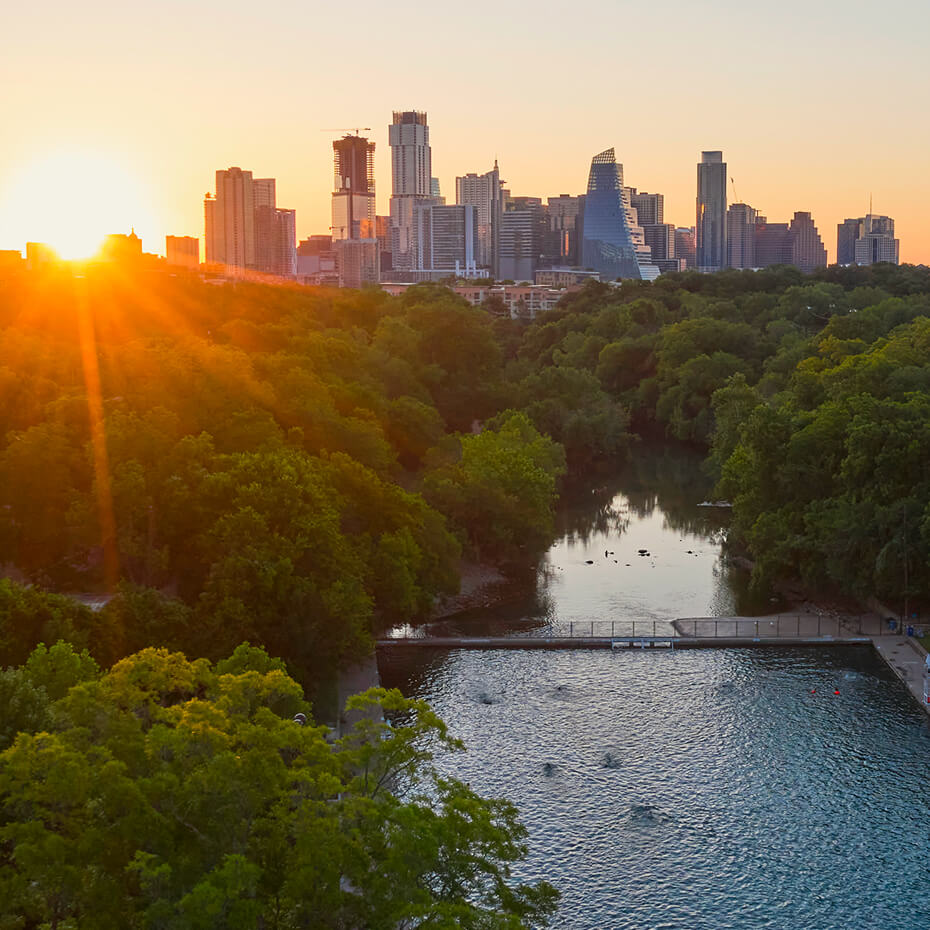 Sunrise over Barton Springs, with the downtown Austin skyline behind the tree-lined shore