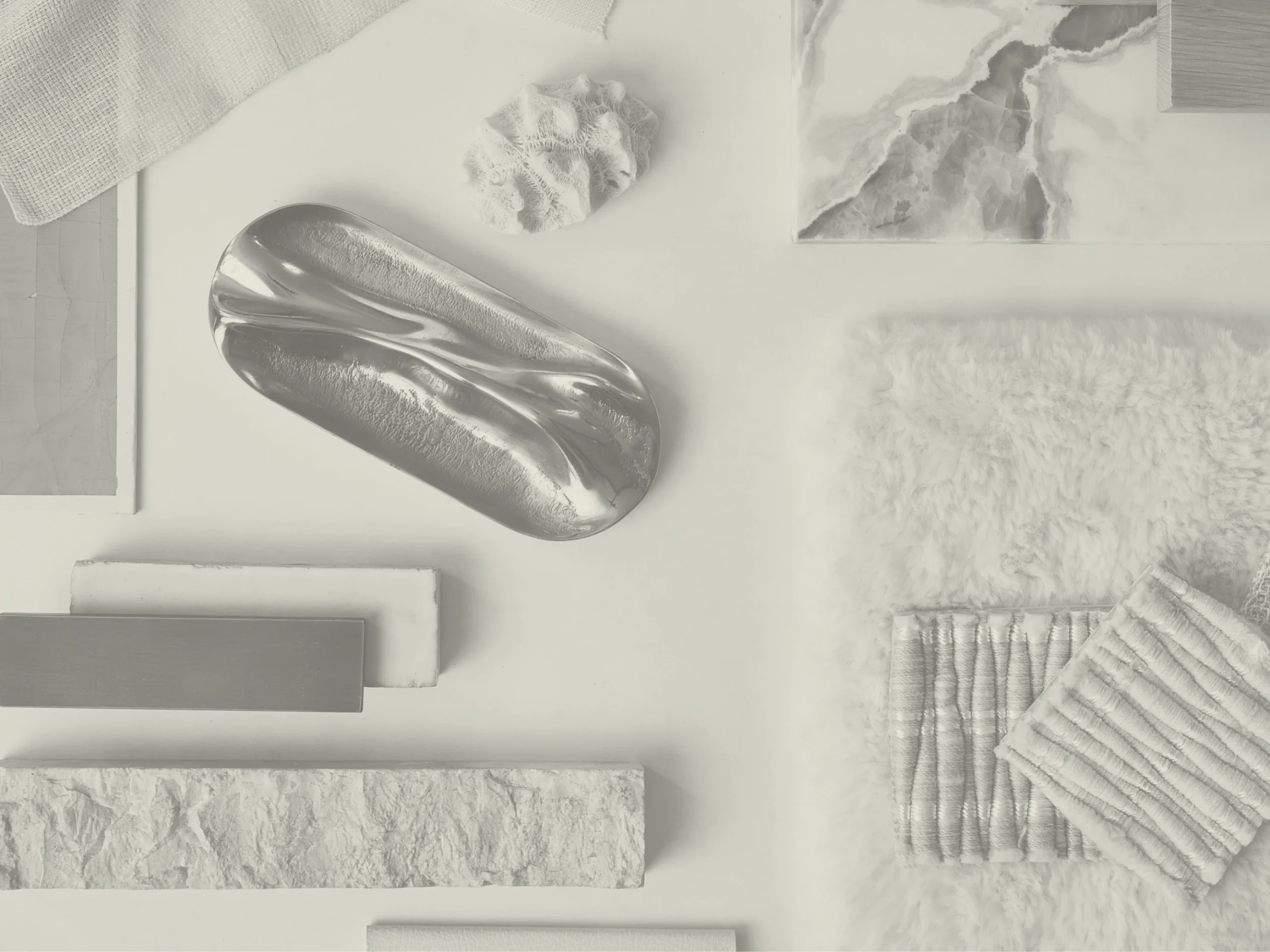 Black and white flat-lay of interior material samples, including polished metal, stone, timber and textured textiles