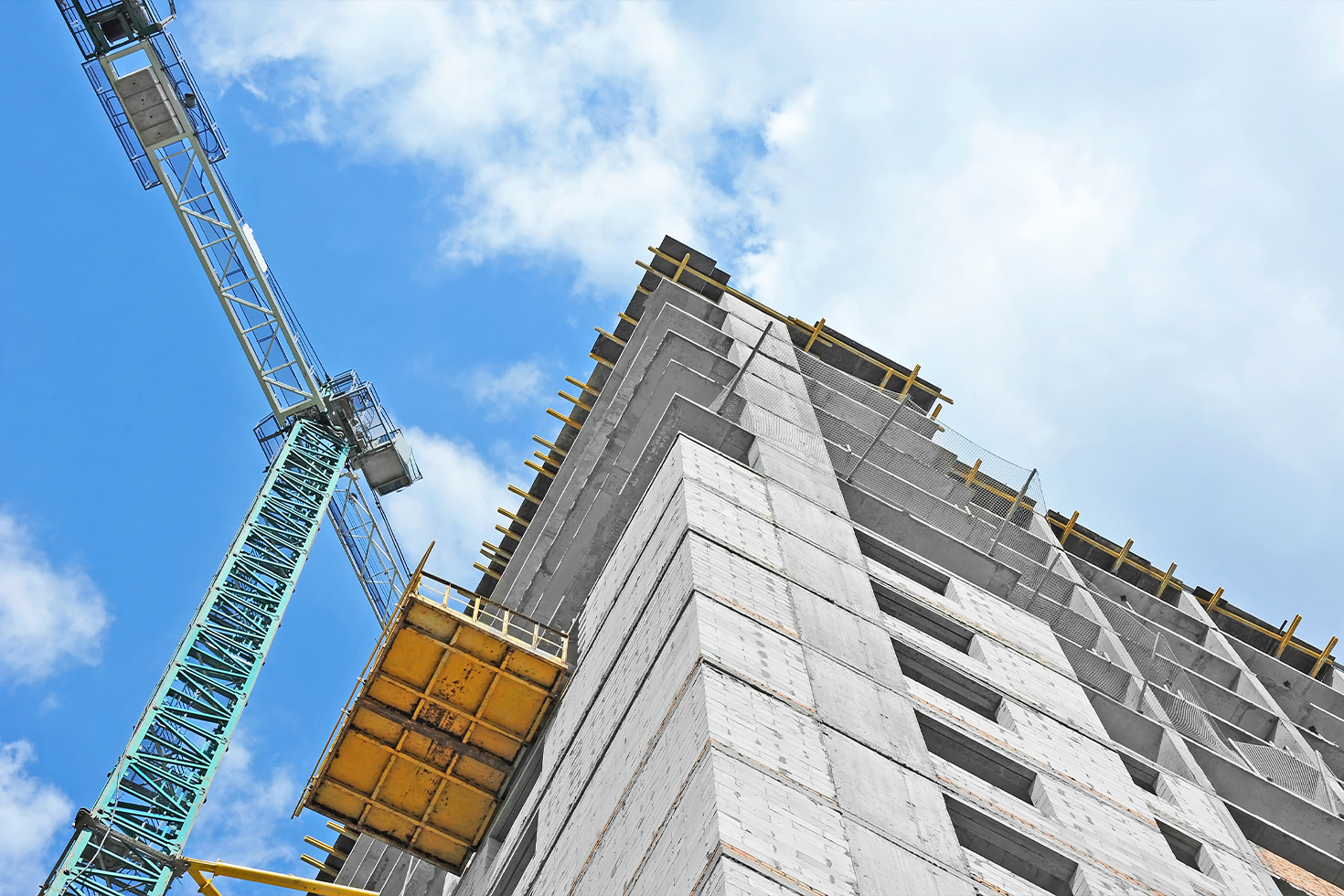 The concrete tower under construction seen from below, with a tower crane and hoist against a clear sky